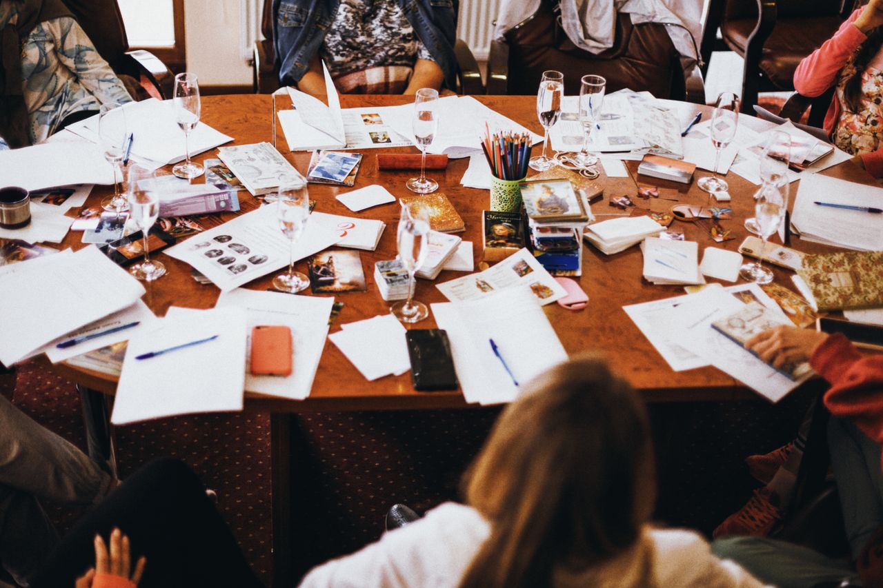 About Group collaborating at a cluttered conference table filled with documents and drinks.
