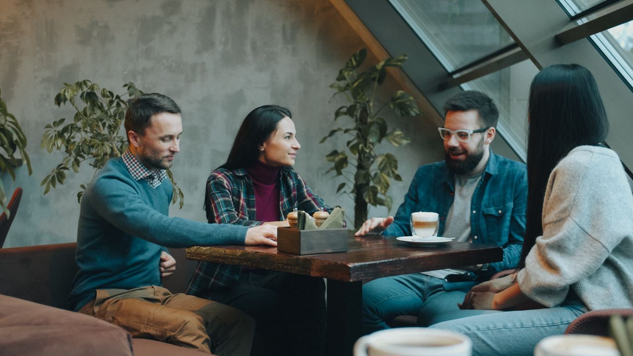 Four adults enjoy coffee and conversation in a modern cafe setting.