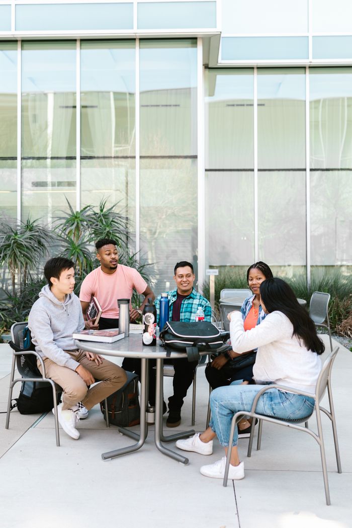 About A diverse group of college students studying together outside a modern building.